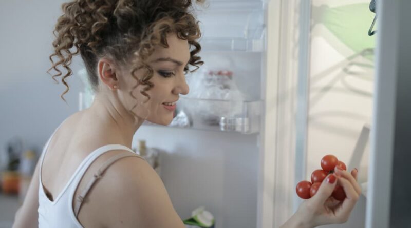 Mulher pegando uma fruta da geladeira